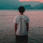 Man standing in the sea wearing an upstream living t-shirt